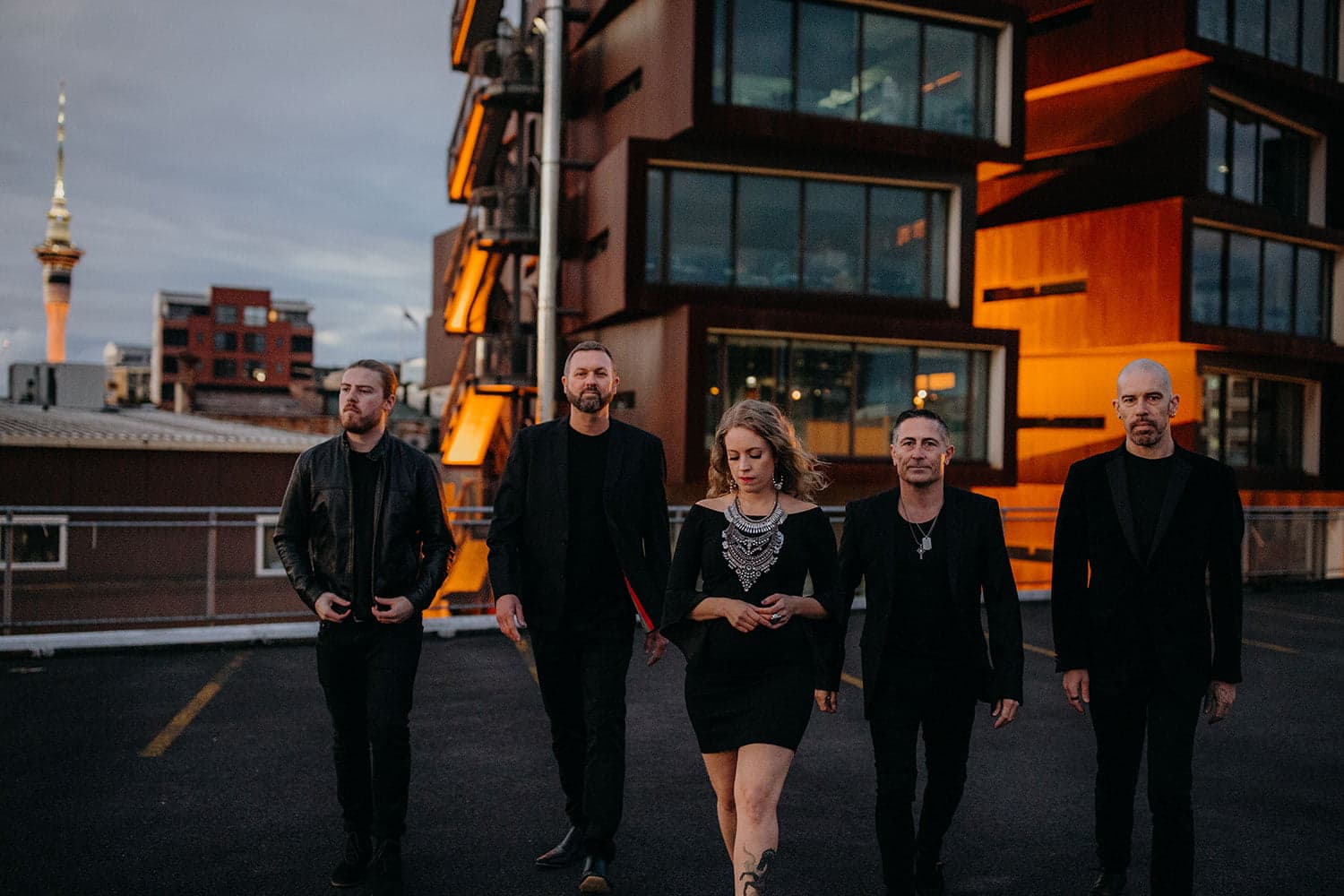Hands Off — Auckland's premier 5-piece covers band walking on a rooftop at golden hour with Sky Tower